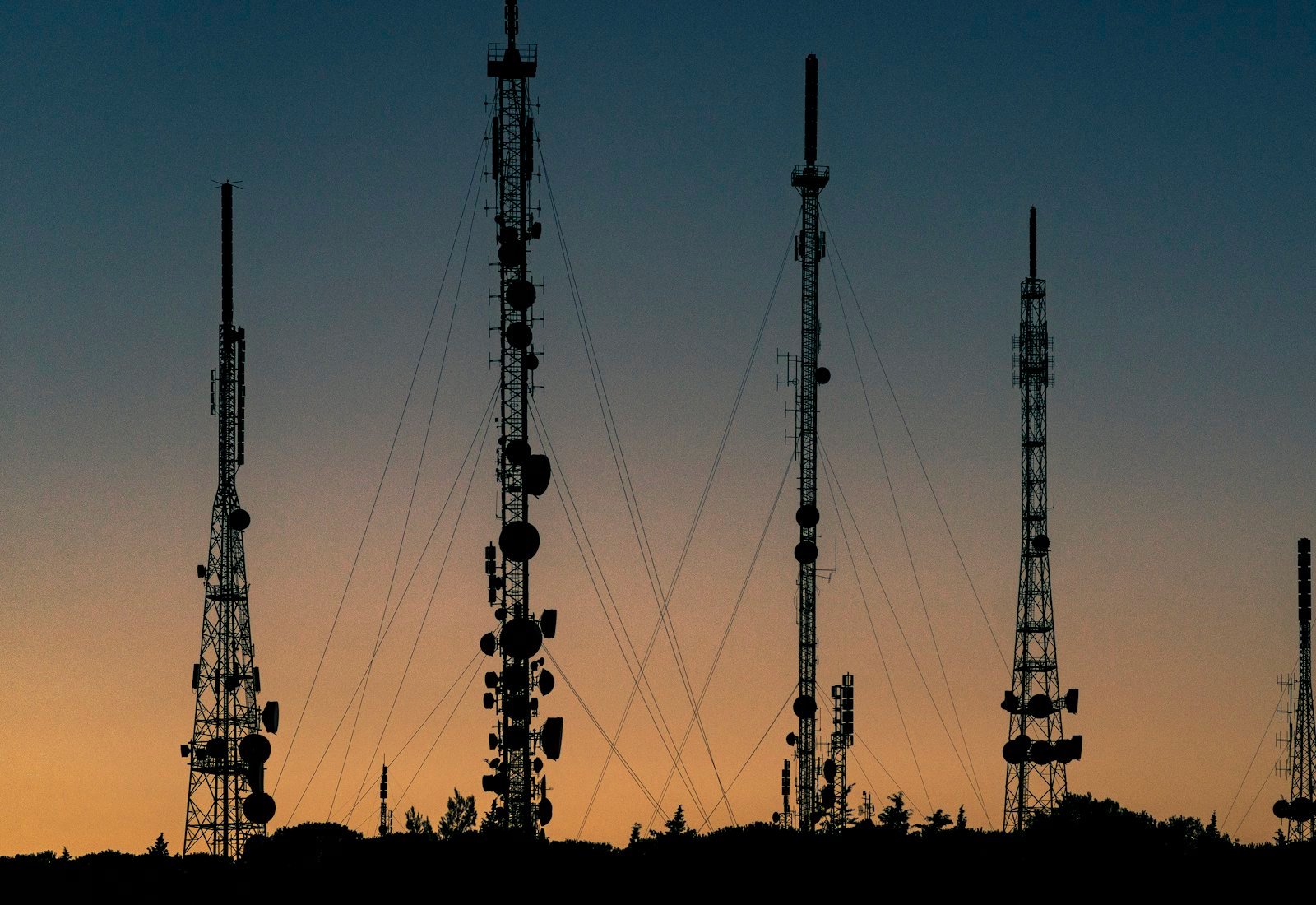 Telecommunications towers silhouetted against an orange sunset
